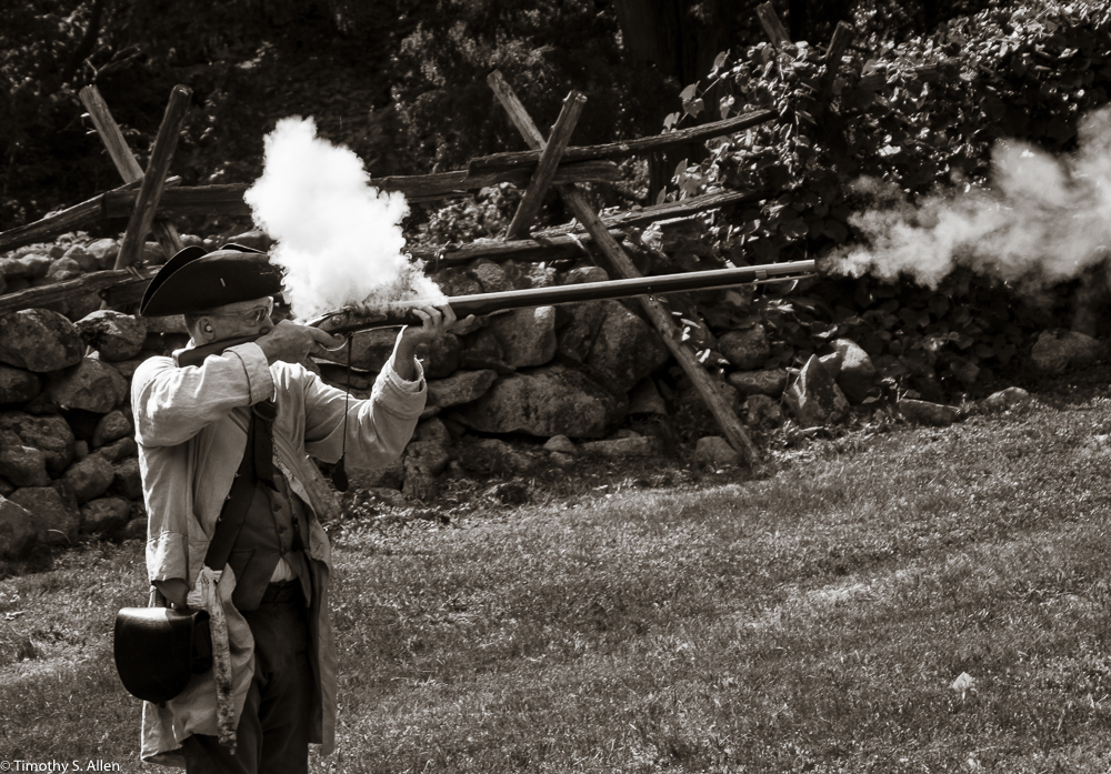 Ed Wilder, a National Park employee in 1775 period clothing firing a musket outside the Hartwell Tavern, Lincoln, MA. August 29, 2015