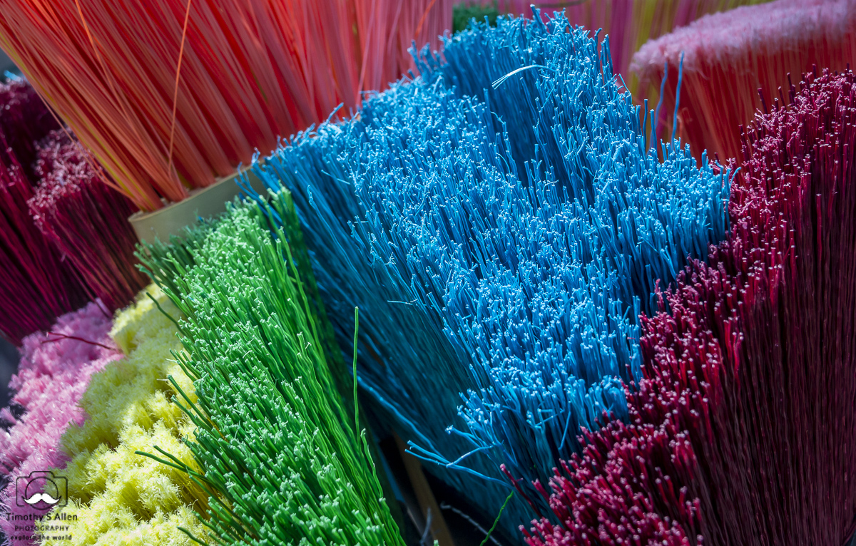 Colorful brooms are displayed with their bristles pointing up. Fulsom Street Flea Market, Sacramento, CA, U.S.A. 08-13-2013.